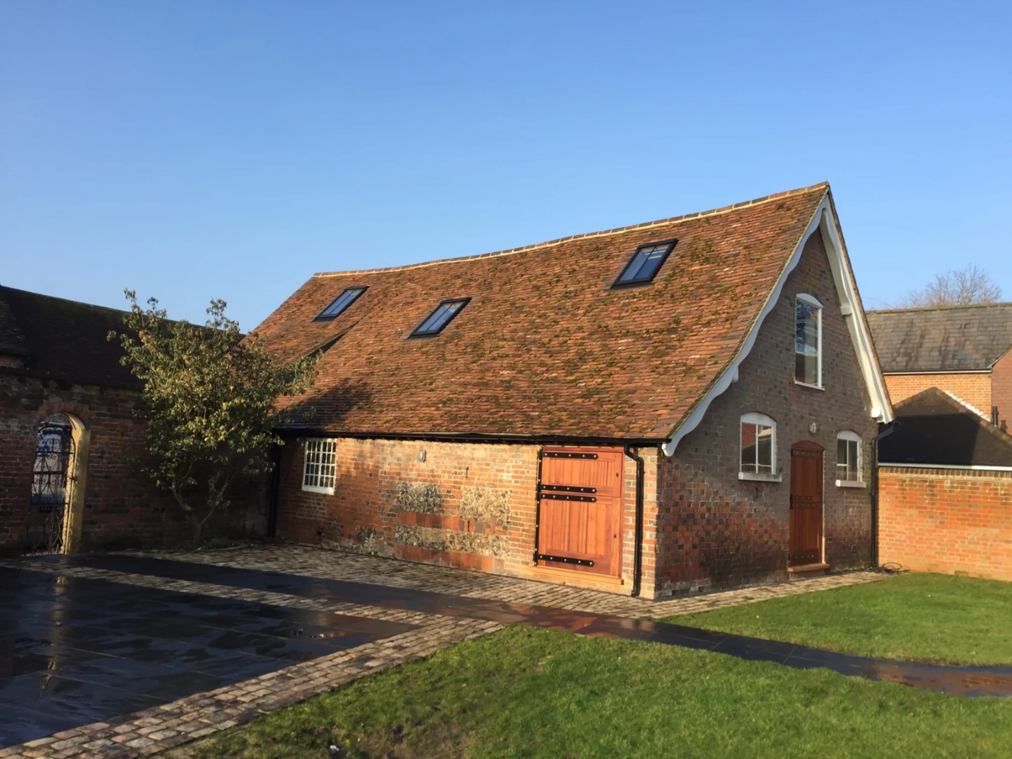 Completed brick and flint barn conversion by Precision Installations, with a clay tiled roof, conservation rooflights, oak doors and a stone paved courtyard