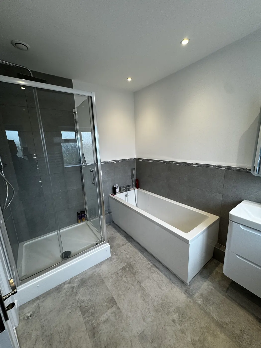 Bathroom with a large-format grey tiled shower enclosure, panelled bath, wall-hung vanity unit and stone-effect tiled floor