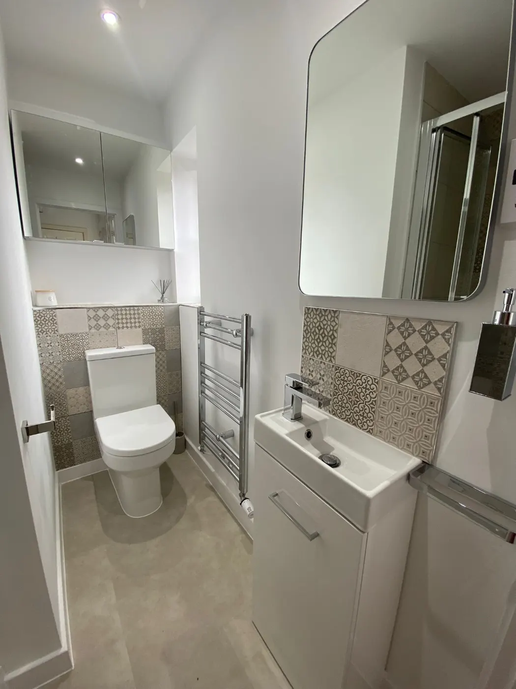 Downstairs cloakroom with a patterned tile splashback, wall-hung basin unit, chrome heated towel rail and recessed mirrored storage