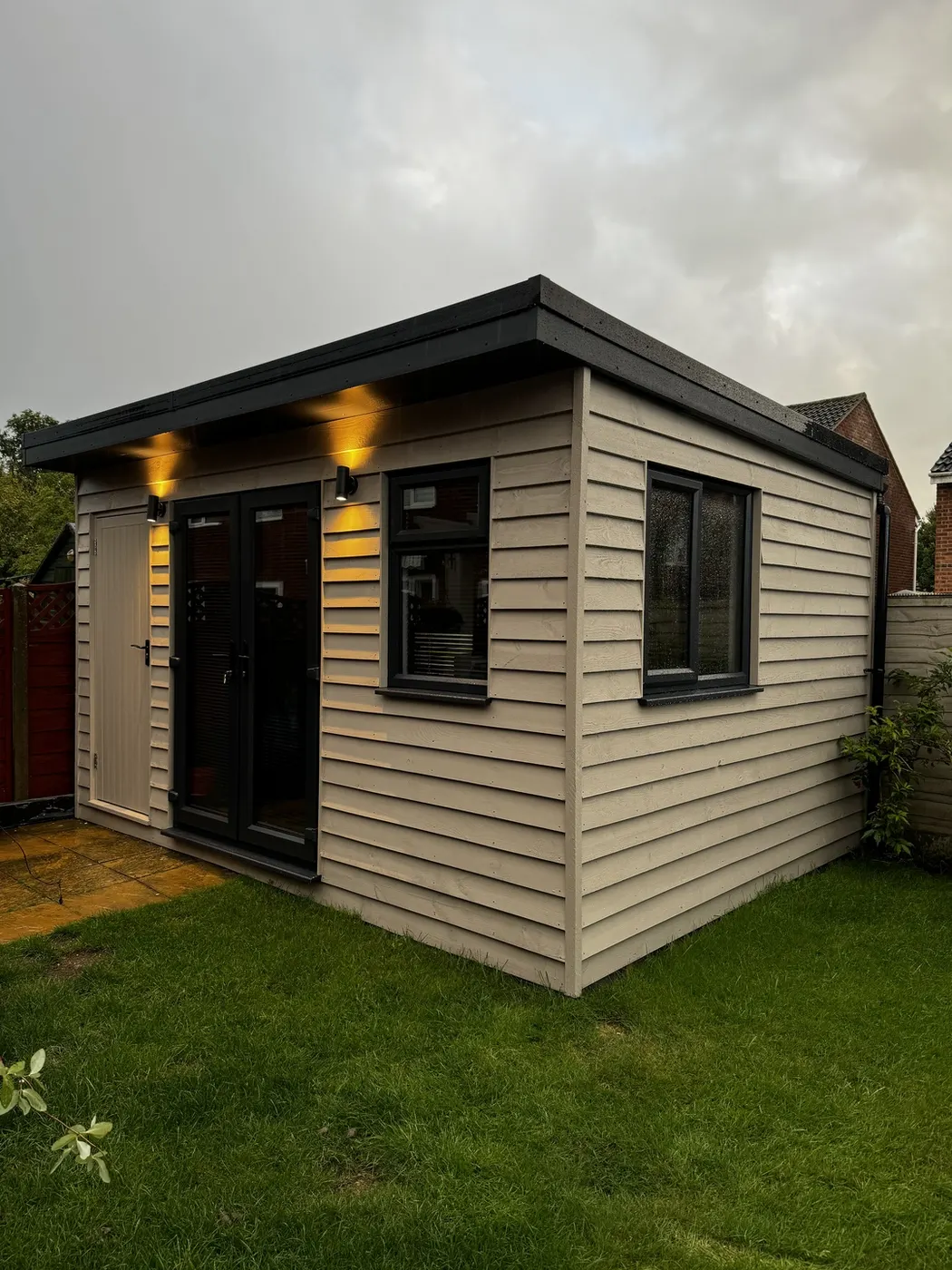 Completed garden room with cream timber cladding, a flat felt roof, anthracite double doors and exterior downlights