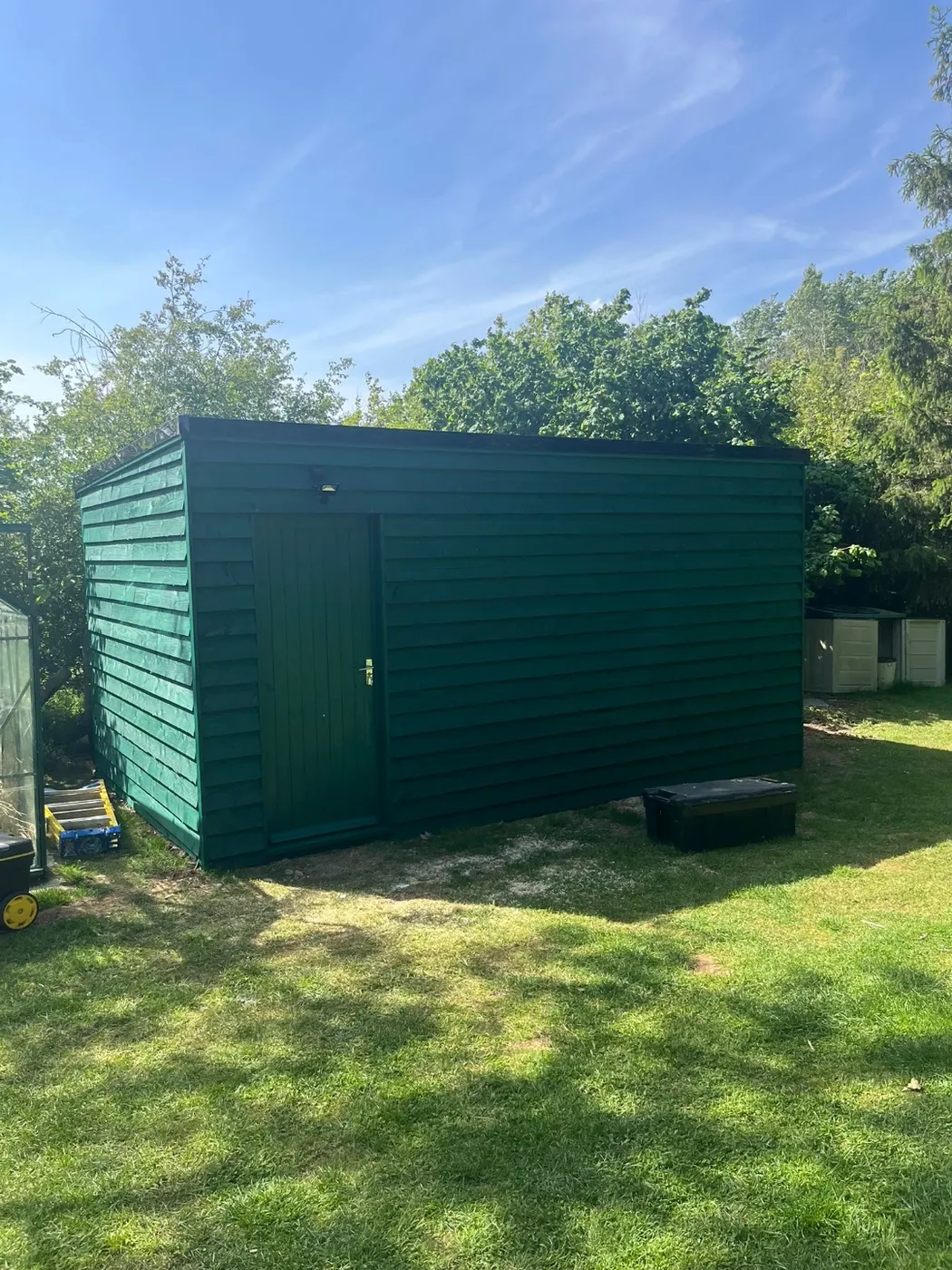 Finished timber garden store with green-painted feather-edge cladding, a flat roof and an exterior light above the door
