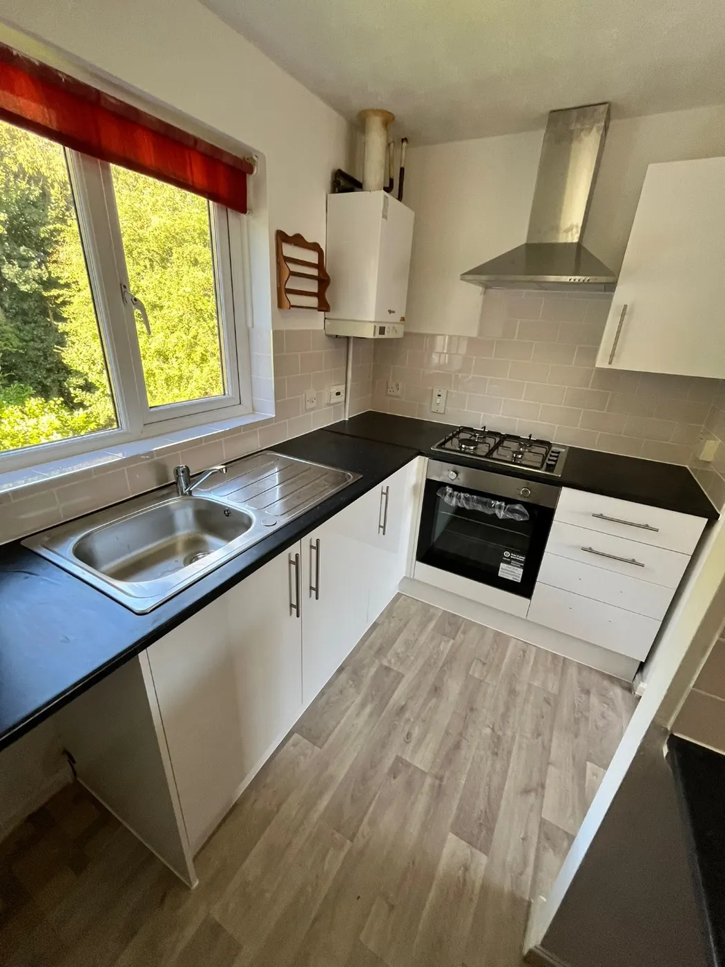 Small white kitchen refit with black worktops, tiled splashback, stainless extractor and new wood-effect flooring