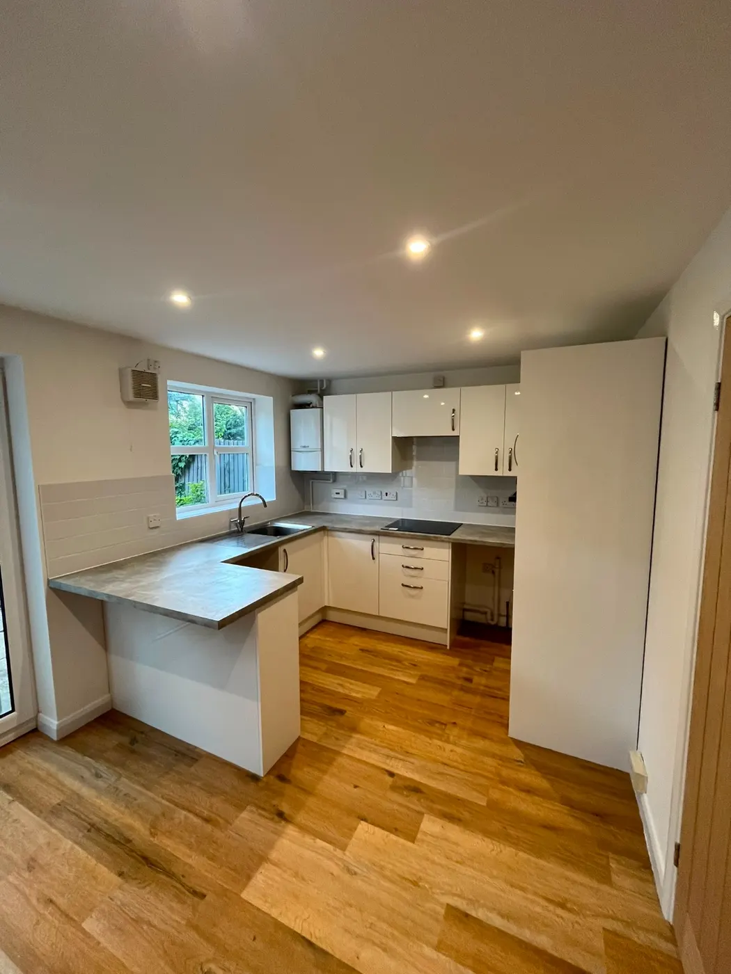 Compact white gloss kitchen with a stone-effect breakfast bar, integrated hob and oak-effect flooring
