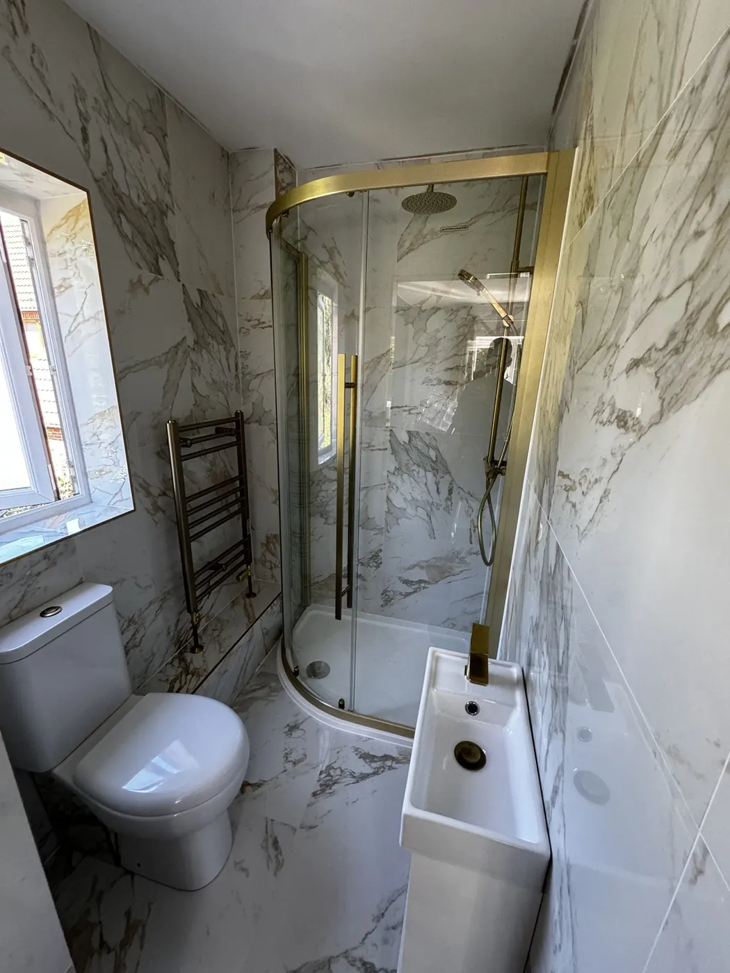 Finished shower room fully tiled in veined marble-effect porcelain with a brushed brass quadrant shower enclosure and matching brassware