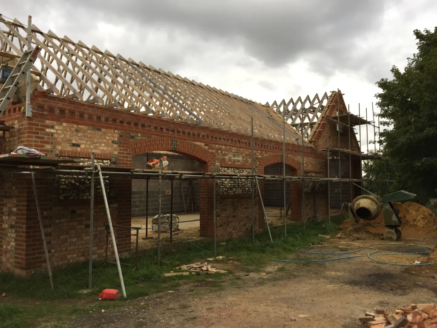 Barn under construction with new brick and flint elevations, brick arch openings, scaffolding and newly fitted roof trusses
