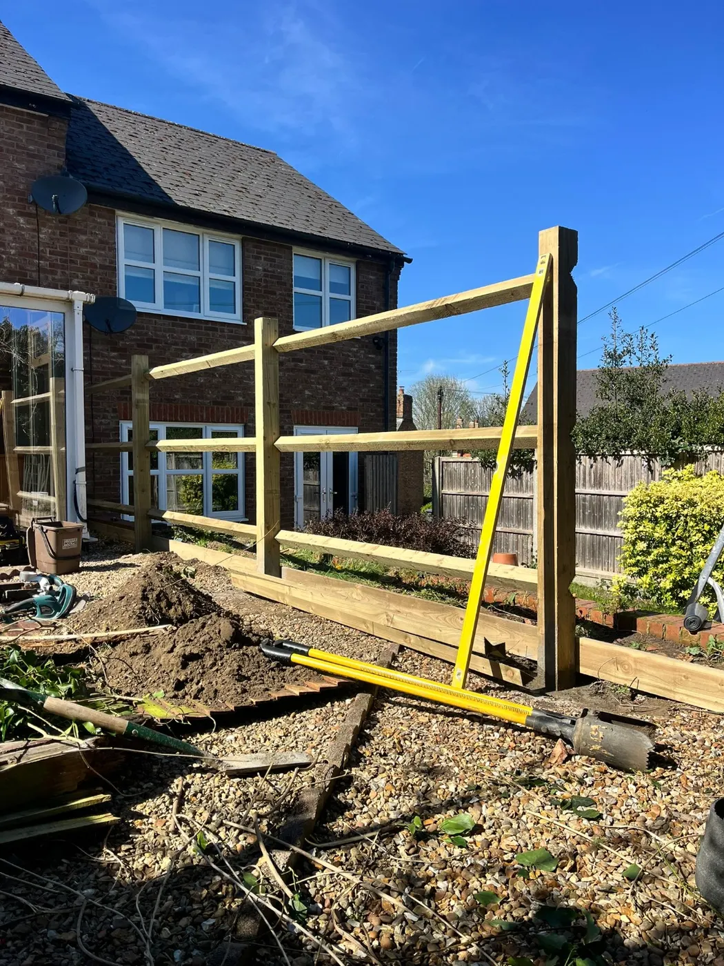 New timber fence posts and rails set out and levelled along a garden boundary during installation