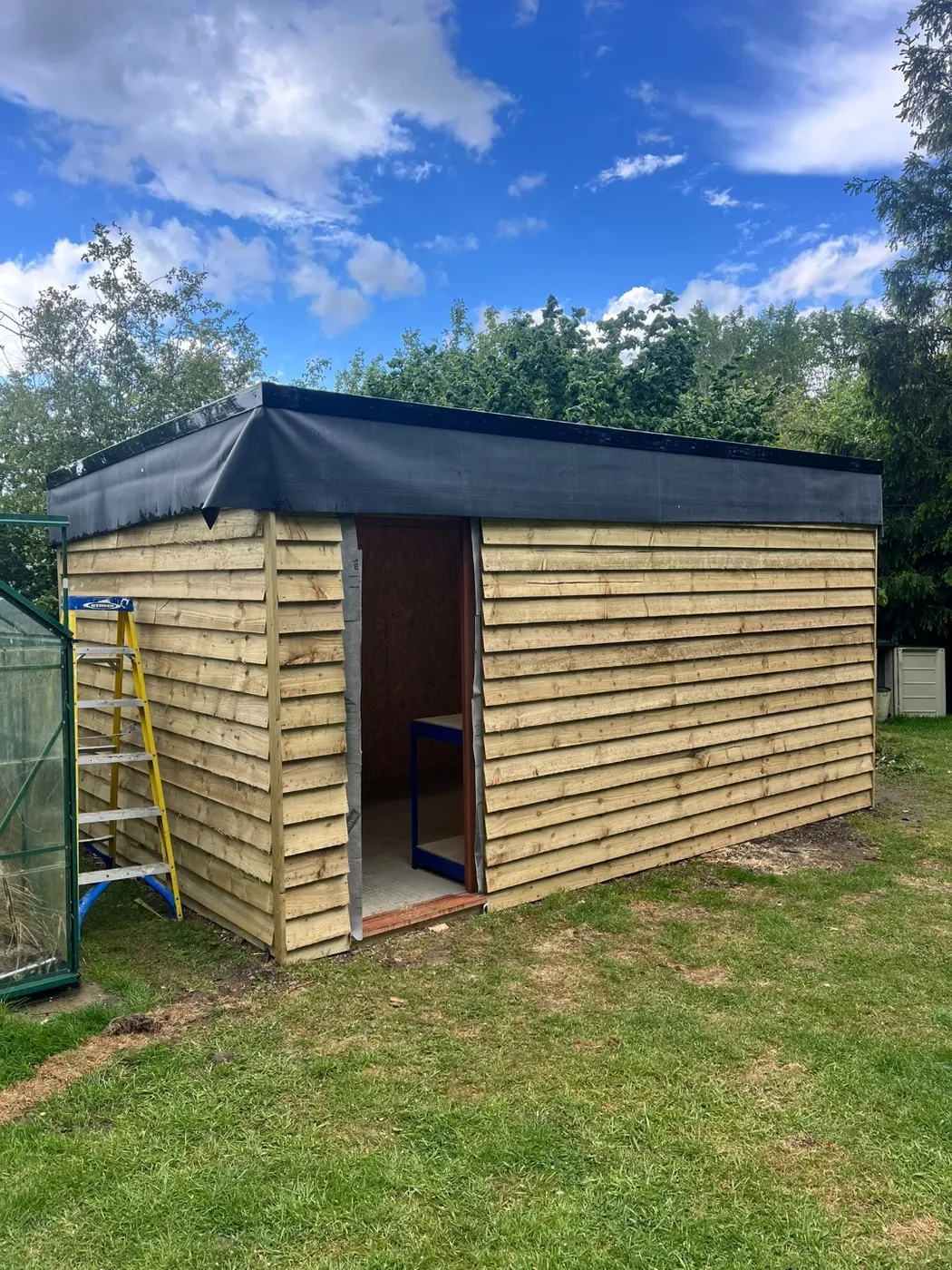 Timber garden store part-built, with feather-edge cladding fixed and the flat roof covered ready for finishing